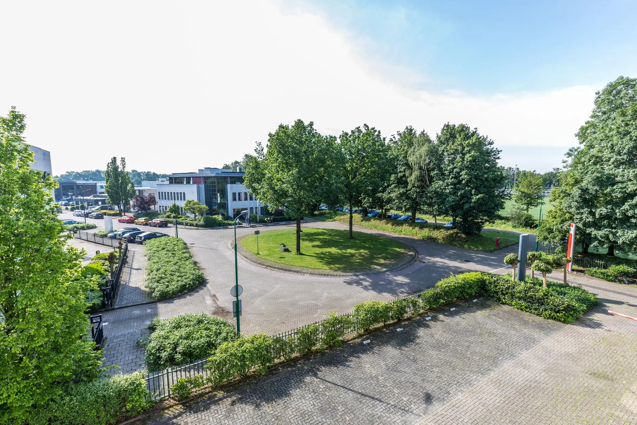 Rondplein met groenstrook en omliggende kantoren aan de Baarnsche Dijk op een zonnige dag.